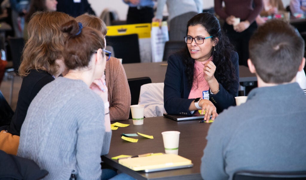 Tanu Mitra speaks with a small group while seated at a table.